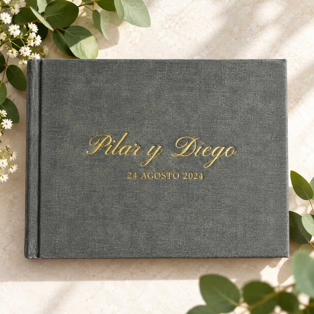 Álbum de fotos de boda forrado en tela gris con los nombres bordados en dorado